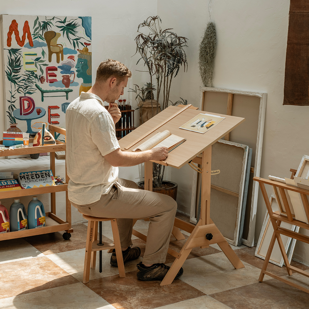 Artist seated and drawing at the angled MEEDEN drafting table
