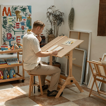 Artist seated and drawing at the angled MEEDEN drafting table